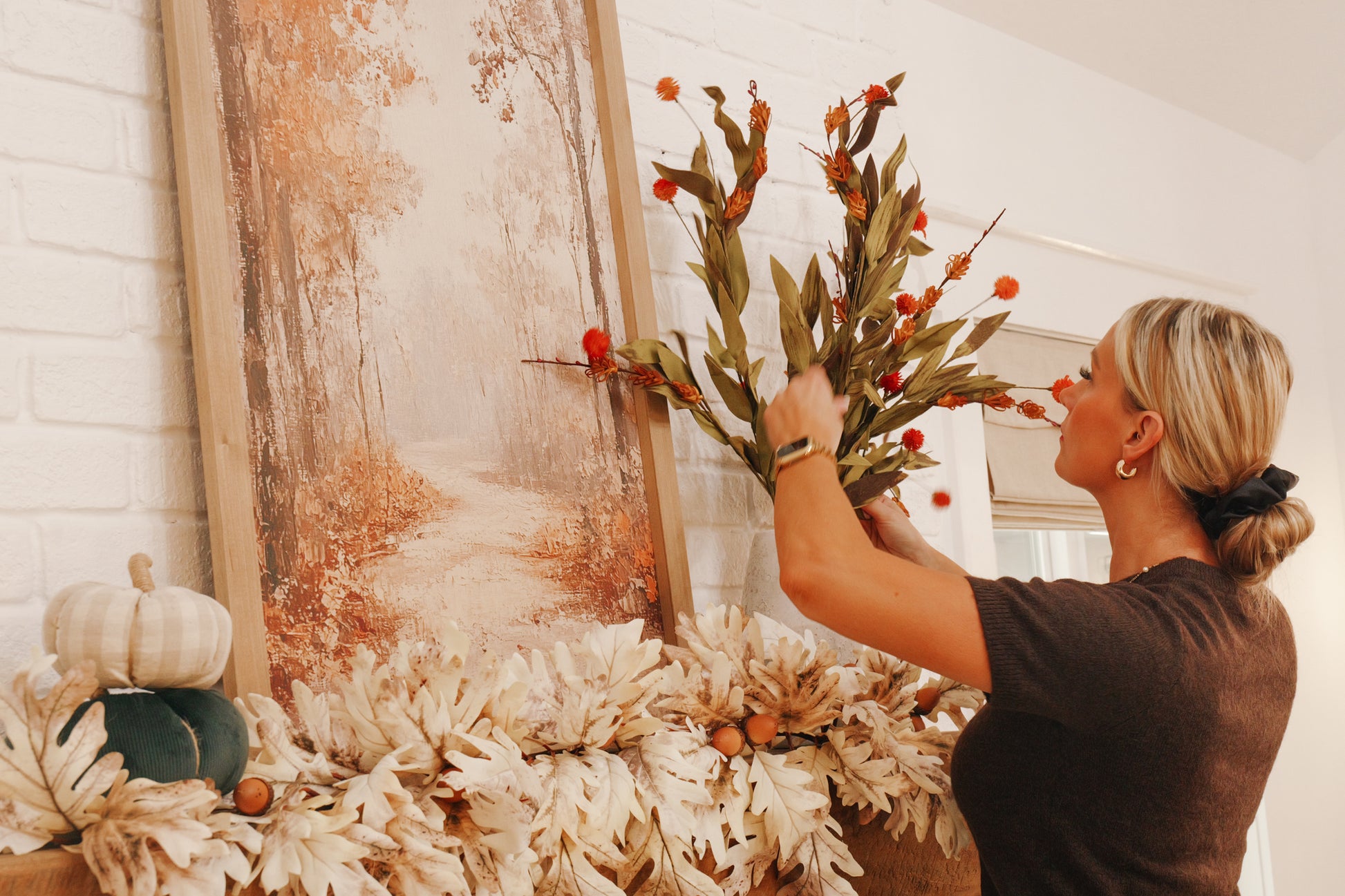 Person arranging flowers on a decorative wall piece with pumpkins and foliage.