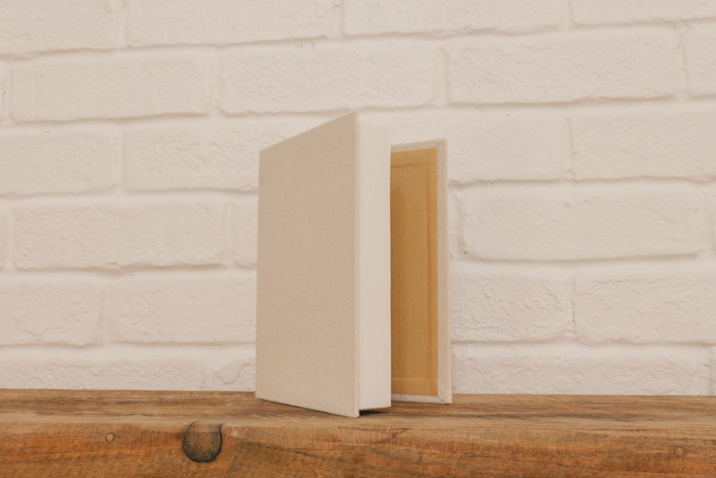 Beige book on a wooden surface with a white brick wall background