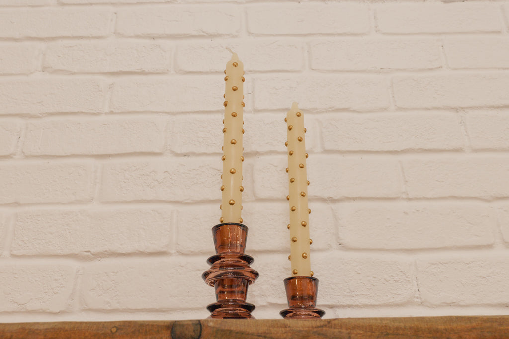 Two candles in decorative holders against a white brick wall.