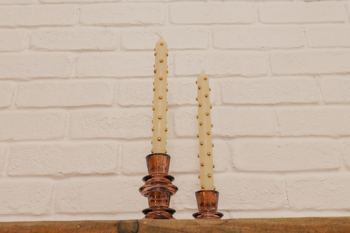 Two candles in decorative holders against a white brick wall.