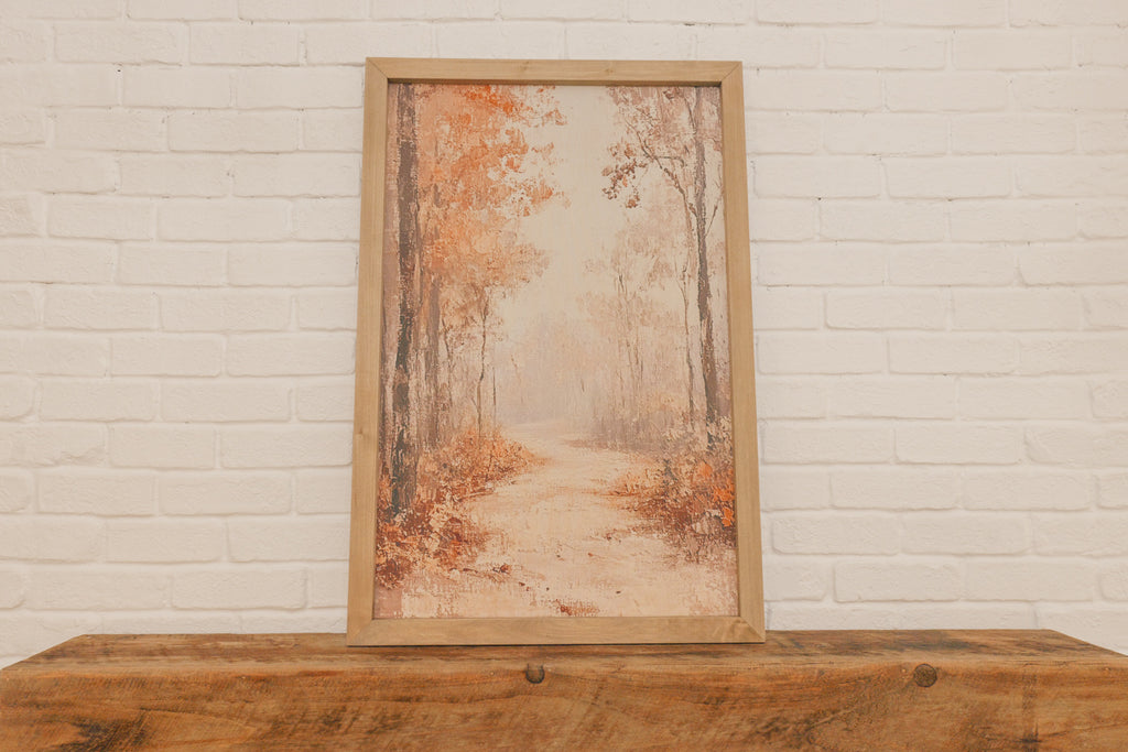 Framed artwork of a forest scene on a wooden surface with a white brick wall background