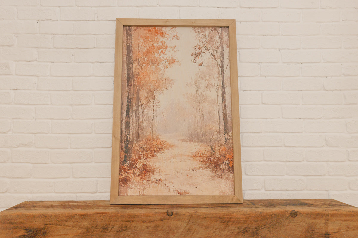 Framed artwork of a forest scene on a wooden surface with a white brick wall background